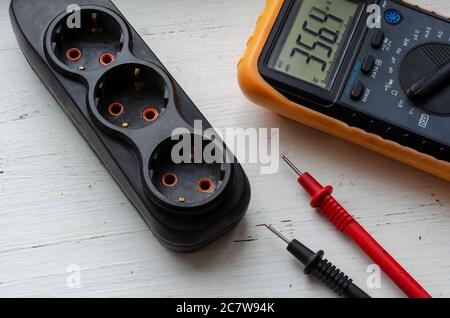 Multimeter and electric splitter on a white wooden background. Measurement of electric network parameters. Electrical safety. Qualified electrician se Stock Photo