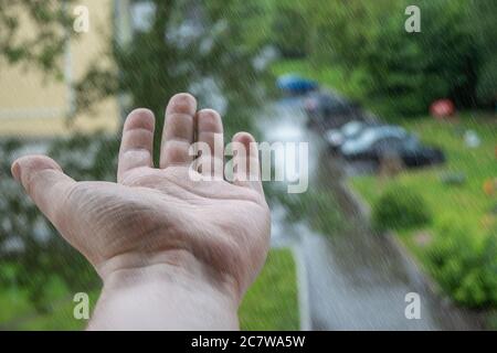 a person hand palm up from the window of a multi storey building on which raindrops are dripping Stock Photo