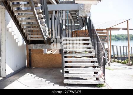 Old metal and concrete stairs with a handrail outside the building near the river at sunny summer day. Architecture background Stock Photo