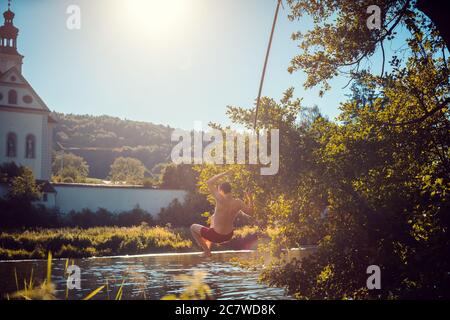 Man swinging on a rope into the water of a river Stock Photo