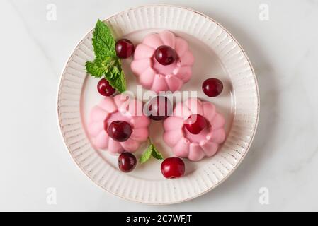 Panna cotta dessert with fresh cherries and mint in a plate. Healthy italian food dessert. top view Stock Photo