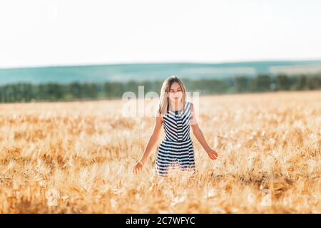 Happy teenage beautiful girl running down golden wheat field at the sunset Stock Photo