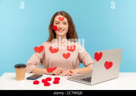 Amazing happy young woman with kind smile sitting at workplace office, all covered with sticker love hearts, full of valentine's day greetings, romanc Stock Photo