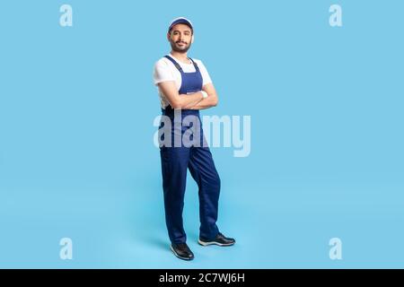 Full length confident professional handyman in overalls standing with crossed hands, smiling at camera. Profession of service industry, house repair. Stock Photo