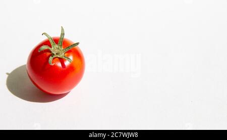 One red cherry tomato with green stems and tough shadow on a white background.copyspace for text Stock Photo