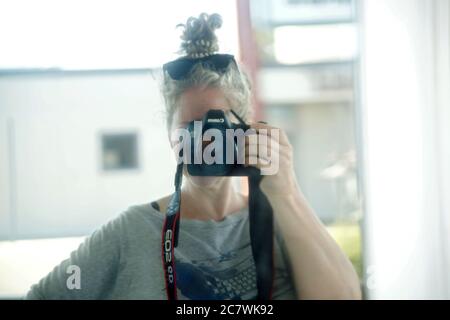 Self-portrait of a female photographer outdoors with a Canon digital camera on a sunny summer day, wearing sunglasses on her head and a blond updo hai Stock Photo
