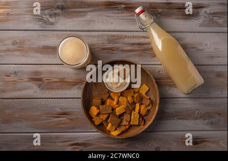 Top view homemade tradishional russian light rye kvass in bottle with glass cup and crackers on wooden background. Wonderful healthy refreshing drink for summer Stock Photo