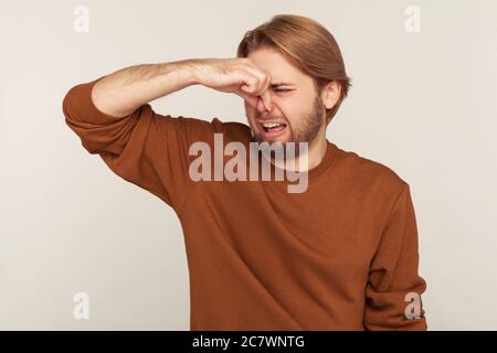 Bad smell. Portrait of bearded man grabbing nose, holding breath and grimacing in disgust, expressing repulsion to stink, fart gases, intolerable odor Stock Photo