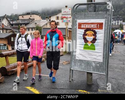 Chamonix, Chamonix Mont Blanc, France. 19th July, 2020. Pedestrians in Chamonix, France walk past a sign with a masked face on it. In this region, the vast majority of visitors, locals, and workers go without masks or wear them improperly. The French Conseil Scientifique has warned of a second wave and the country will be imposing a stricter mask regulation. If it will be accepted remains to be seen. Credit: Sachelle Babbar/ZUMA Wire/Alamy Live News Stock Photo