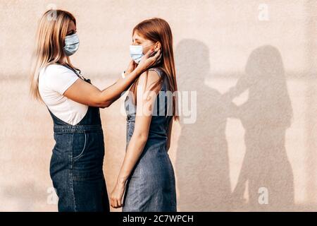 Young mom helping her daughter to put on a medical mask. Corona virus outbreak, protection measures. Copy space Stock Photo