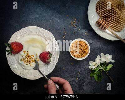 Yoghurt with bee pollen grains, strawberry and honey in white ceramic bowl. Stock Photo