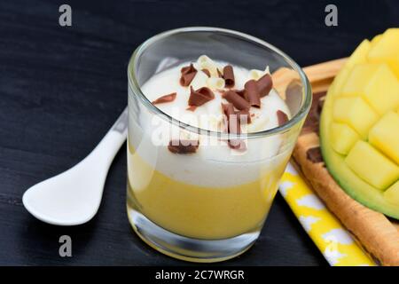 Mousse of mango with chocolate in a glass and mango cubes on black wood table Stock Photo