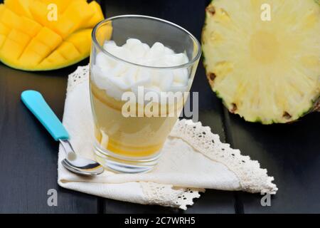 Mousse of mango fruit and pineapple in a glass jar on black wood table Stock Photo