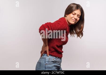 Unhealthy girl in shaggy sweater touching sore back, feeling acute pain, suffering kidney inflammation, pinched nerve, discomfort lower lumbar muscula Stock Photo