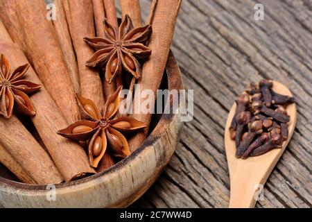 Cinnamon sticks with star anise in a bowl and cloves in a wooden spoon on table Stock Photo