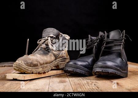 Old work shoe pierced with a nail. New work shoes. Dark background. Stock Photo