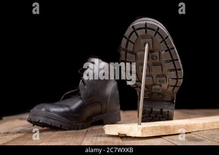 New work shoes pierced with a metal nail. Accidents at work of construction workers. Dark background. Stock Photo