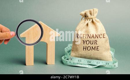 Money bag with the words Refinance your home and miniature house. Real estate concept. Business and finance. Mortgage, loan. Interest rates. Home Lend Stock Photo