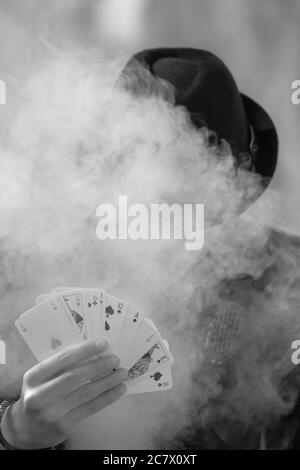 Grayscale portrait of a mystical male gamer's hand holding poker cards with smoke in the foreground Stock Photo