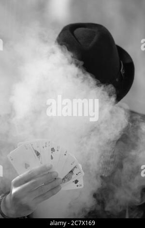 Grayscale portrait of a mystical male gamer's hand holding poker cards with smoke in the foreground Stock Photo