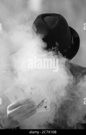 Grayscale portrait of a mystical male gamer's hand holding poker cards with smoke in the foreground Stock Photo