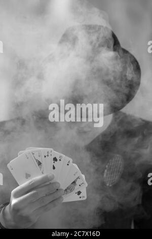 Grayscale portrait of a mystical male gamer's hand holding poker cards with smoke in the foreground Stock Photo