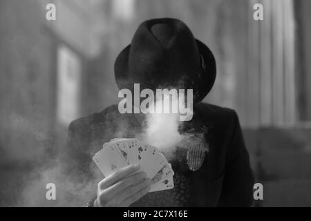 Grayscale portrait of a mystical male gamer's hand holding poker cards with smoke in the foreground Stock Photo