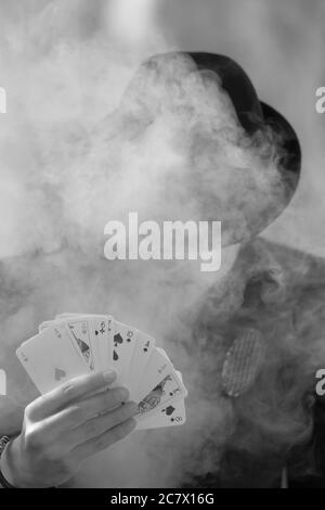 Grayscale portrait of a mystical male gamer's hand holding poker cards with smoke in the foreground Stock Photo