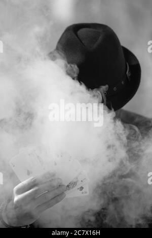 Grayscale portrait of a mystical male gamer's hand holding poker cards with smoke in the foreground Stock Photo