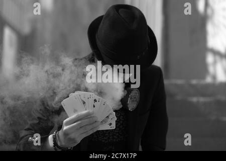 Grayscale portrait of a mystical male gamer's hand holding poker cards with smoke in the foreground Stock Photo