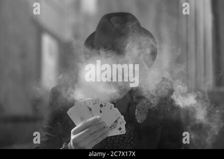 Grayscale portrait of a mystical male gamer's hand holding poker cards with smoke in the foreground Stock Photo