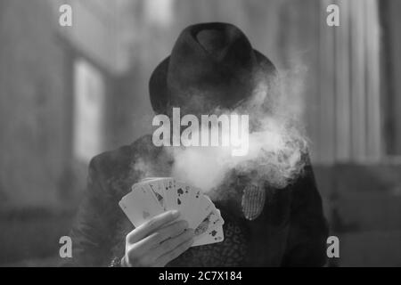 Grayscale portrait of a mystical male gamer's hand holding poker cards with smoke in the foreground Stock Photo