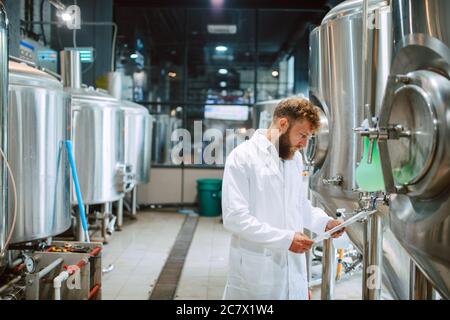 Caucasian male  technologist expert in white suit  operating production machine in food factory and doing quality control and holding checklist Stock Photo
