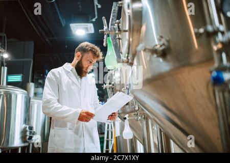 Caucasian male  technologist expert in white suit  operating production machine in food factory and doing quality control and holding checklist Stock Photo