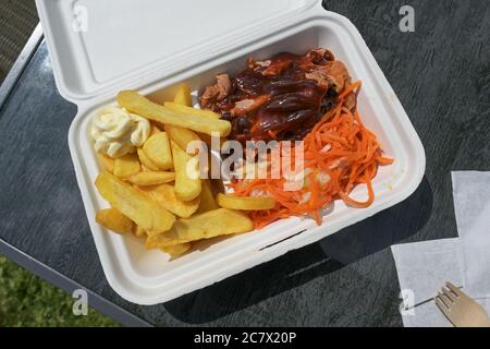 Fast food to go in a box with pulled pork, coleslaw and carrot salad, french fries, barbecue sauce and mayonnaise, high angle view from above, Stock Photo