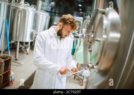Caucasian male  technologist expert in white suit  operating production machine in food factory and doing quality control and holding checklist Stock Photo