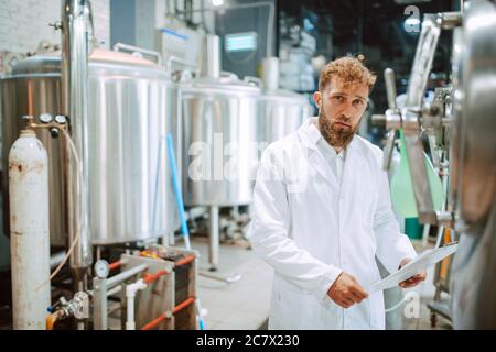 Caucasian male  technologist expert in white suit  operating production machine in food factory and doing quality control and holding checklist Stock Photo
