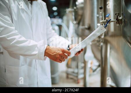 Caucasian male  technologist expert in white suit  operating production machine in food factory and doing quality control and holding checklist Stock Photo