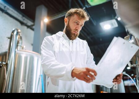 Caucasian male  technologist expert in white suit  operating production machine in food factory and doing quality control and holding checklist Stock Photo