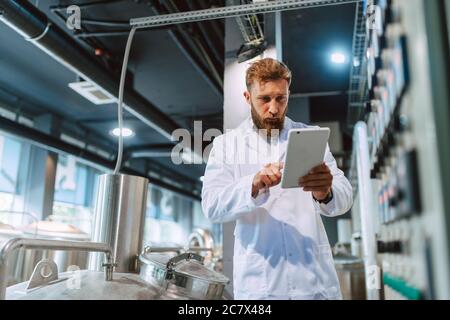 Professional caucasian handsome technologist expert in white uniform standing in pharmaceutical or food factory  - production plant checking producti Stock Photo