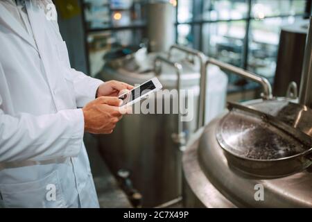 Closeup of tablet computer in hand of professional caucasian technologist expert in white uniform  in production plant - food or drink factory Stock Photo