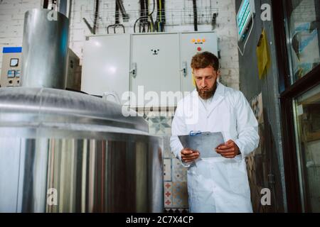 Caucasian male  technologist expert in white suit  operating production machine in food factory and doing quality control and holding checklist Stock Photo