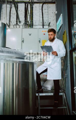 Caucasian male  technologist expert in white suit  operating production machine in food factory and doing quality control and holding checklist Stock Photo