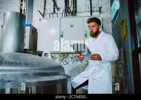 Caucasian male  technologist expert in white suit  operating production machine in food factory and doing quality control and holding checklist Stock Photo