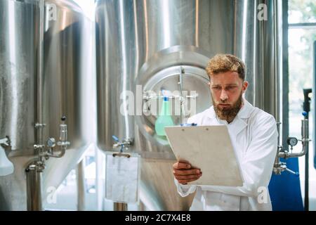 Caucasian male  technologist expert in white suit  operating production machine in food factory and doing quality control and holding checklist Stock Photo