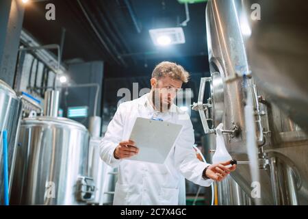 Caucasian male  technologist expert in white suit  operating production machine in food factory and doing quality control and holding checklist Stock Photo