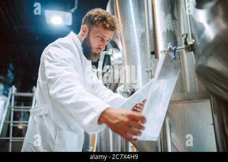 Caucasian male  technologist expert in white suit  operating production machine in food factory and doing quality control and holding checklist Stock Photo