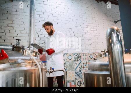 Caucasian male  technologist expert in white suit  operating production machine in food factory and doing quality control and holding checklist Stock Photo