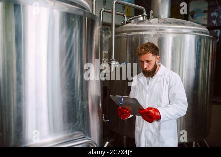 Caucasian male  technologist expert in white suit  operating production machine in food factory and doing quality control and holding checklist Stock Photo