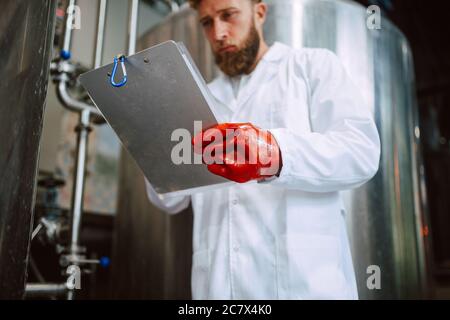 Caucasian male  technologist expert in white suit  operating production machine in food factory and doing quality control and holding checklist Stock Photo